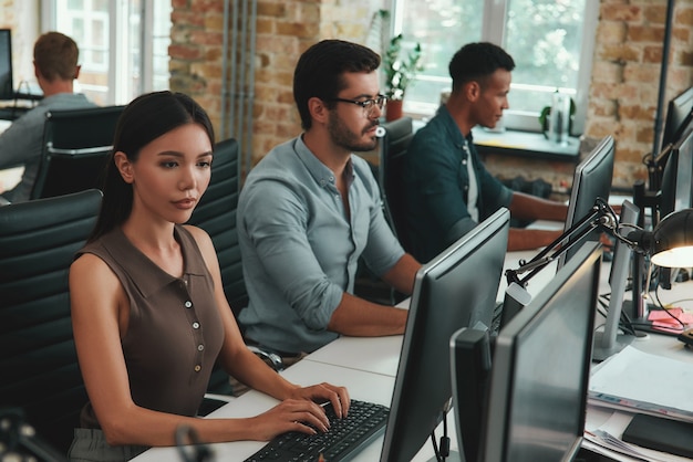 Foto grupo de rutina diaria de jóvenes empleados que trabajan en computadoras mientras están sentados en un espacio abierto moderno