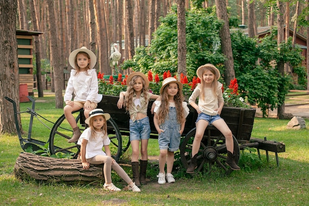 Grupo de simpáticas niñas preadolescentes posando junto a un carro de madera vintage diseñado como lecho de flores al aire libre