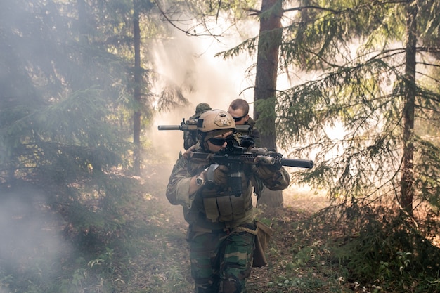 Grupo de soldados armados con trajes de camuflaje sosteniendo rifles y cruzando el bosque neblinoso