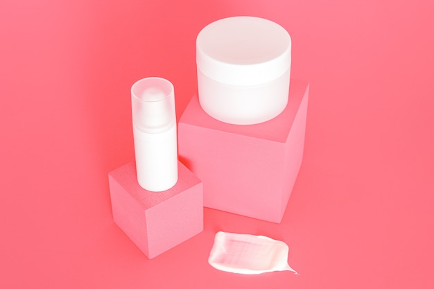 Grupo de tarros de crema cosmética sin marca blanca de pie en podios de color rosa. Presentación de productos para el cuidado de la piel sobre fondo rosa. Maqueta de moda. Cuidado de la piel, belleza y spa.