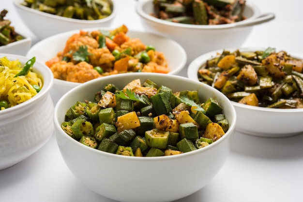 Grupo de tawa fry sabzi o sabji como coliflor o Phool Gobhi, bhindi O okra, Gwar O frijoles en racimo, frijoles franceses, repollo o Patta Gobi, frijoles verdes planos, servidos en un tazón. enfoque selectivo