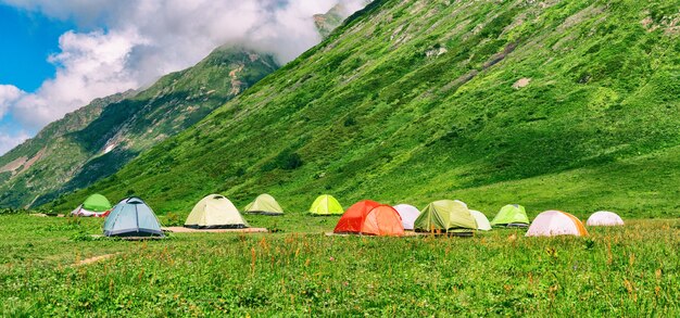 Grupo de tiendas de campaña de colores en el camping en el fondo de las montañas y el cielo nublado