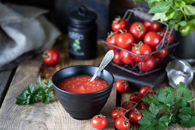 Grupo de tomates cherry rojos como ingrediente para la salsa de tomate en un recipiente negro sobre una mesa de madera.