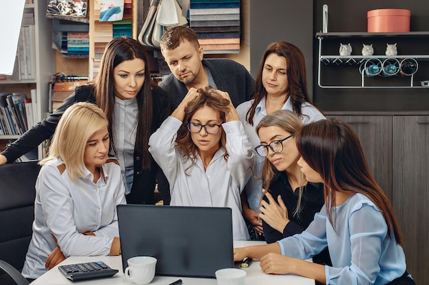 Grupo de trabajadores trabajando duro y analizando un proyecto en una computadora portátil. La chica encantadora con gafas está muy emocionada y se aferra a su cabello. Concepto de observación