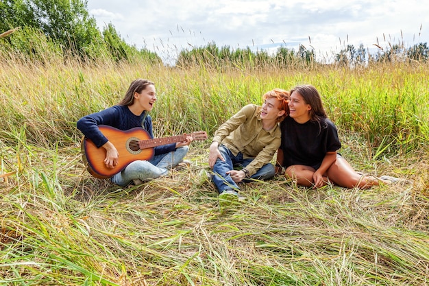 Grupo de tres amigos chico y dos chicas con guitarra cantando canción