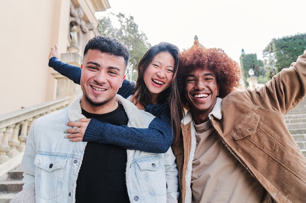 Foto grupo de tres jóvenes amigos multirraciales divirtiéndose y sonriendo mirando la cámara frente a la vista de