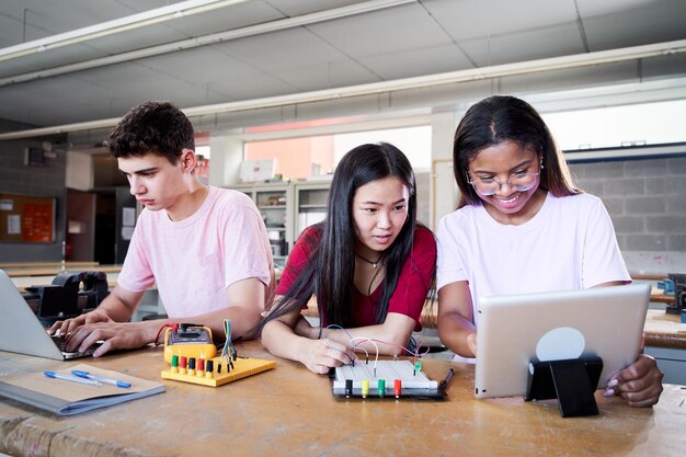 Grupo de tres jóvenes estudiantes de una escuela secundaria técnica que realizan un proyecto de equipo tecnológico