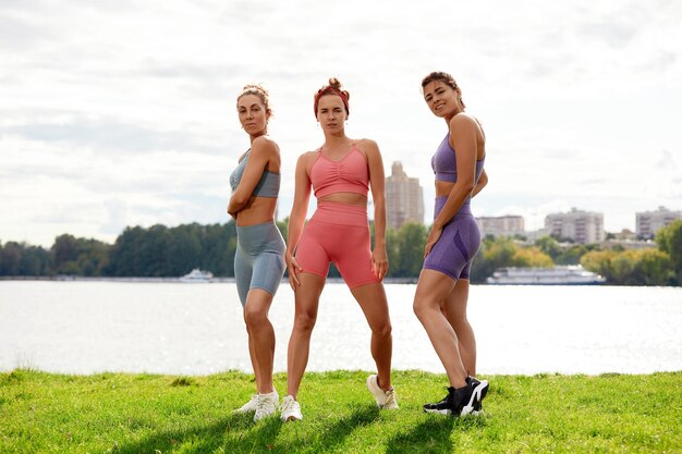 Grupo de tres mujeres se calienta en el parque antes de trotar Concepto de estilo de vida saludable Amigas deportivas divirtiéndose y haciendo diferentes ejercicios de estiramiento en el parque de verano