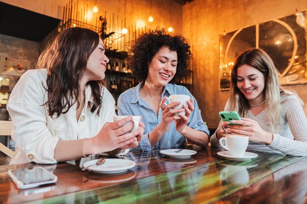 Grupo de tres mujeres jóvenes sonriendo y tomando un café en un restaurante amigos de mujeres multiétnicas