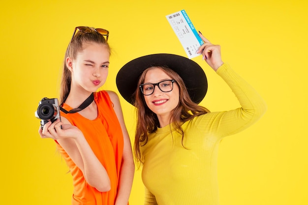 grupo de tres niñas riendo con pasaportes y boletos con cámara fotográfica envuelta en la bandera estadounidense fiesta de primavera estilo verano estudio de fondo amarillo, visa y día de la independencia de estados unidos