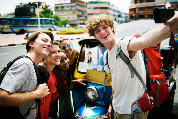 Un grupo de turistas caucásicos tomando autofotos frente a un tuk tuk.