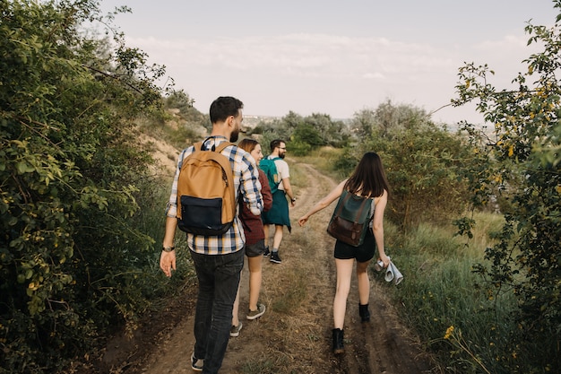 Grupo de turistas con mochilas de senderismo en las montañas, caminando por un camino de tierra.