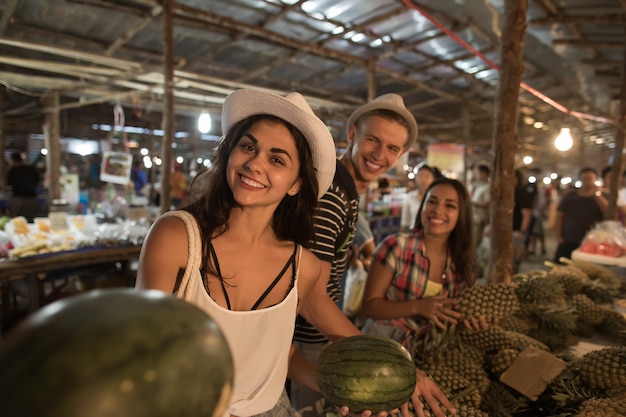 Grupo de turistas que compran sandía en un mercado callejero en Tailandia Jóvenes que compran frutas frescas