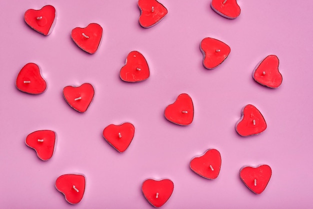 Grupo de velas aromáticas en forma de corazón apagadas en un fondo rosa