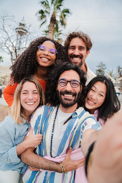 Foto grupo vertical de jóvenes adultos multirraciales sonriendo tomando una selfie juntos para compartir en el