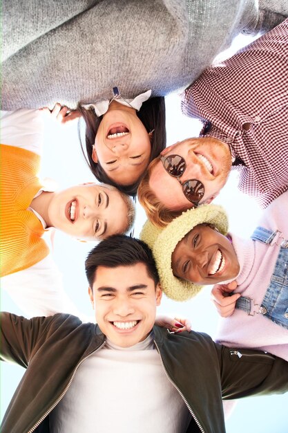 Grupo vertical multirracial y diverso de amigos abrazándose en círculo y mirando hacia abajo a la cámara