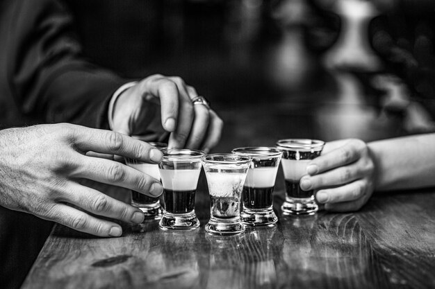 Grupos de amigos copos de tequila no bar Mãos masculinas copos de shot ou licor Amigos bebem shot ou liqueur preto e branco