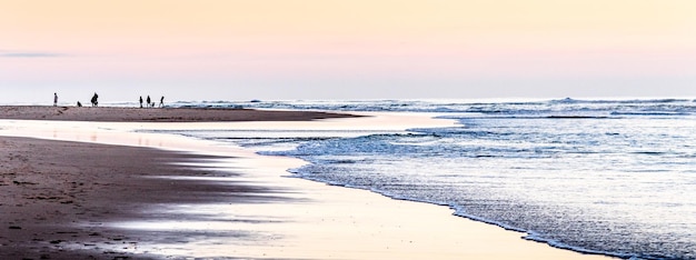 Grupos de caminhantes criam silhuetas que se destacam na luz do pôr do sol em uma praia