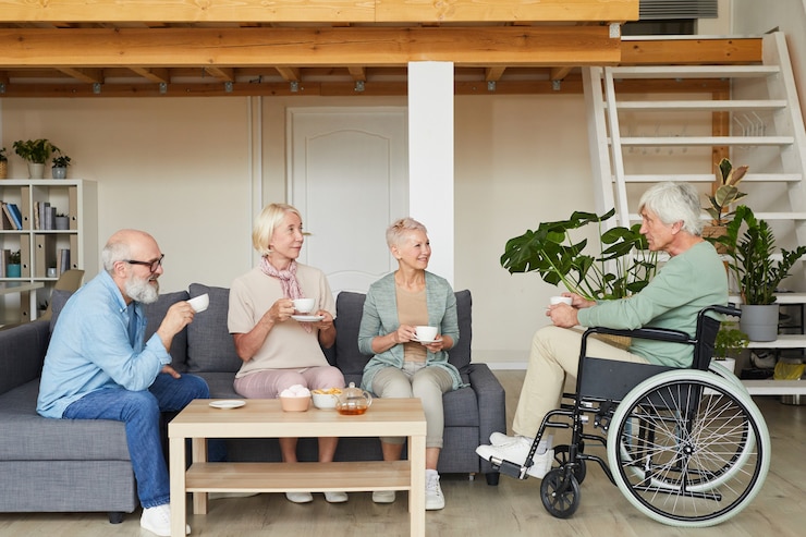Gruppe älterer Freunde, die mit behinderten Mann sprechen und zusammen Tee im Wohnzimmer trinken