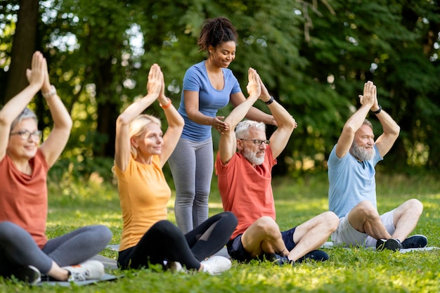 Gruppe aktiver älterer Menschen, die einen Yoga-Kurs im Freien mit einem Ausbilder besuchen