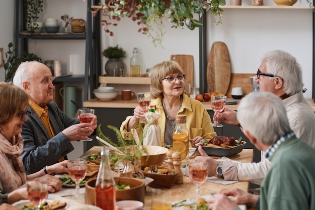 Gruppe alter Freunde, die am Esstisch sitzen und Wein trinken, während sie den Urlaub zu Hause gemeinsam feiern