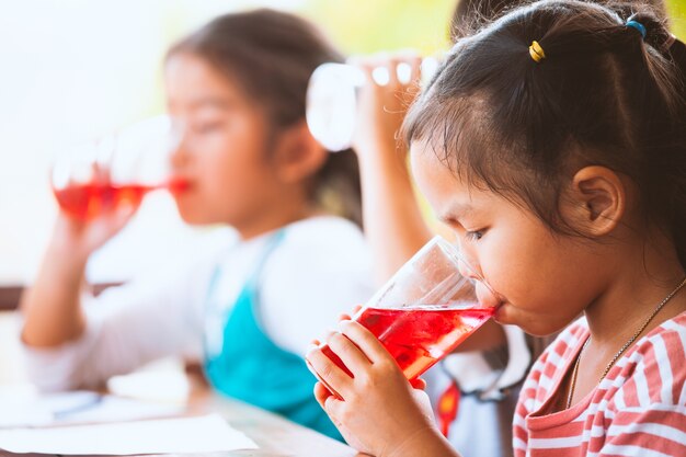 Gruppe asiatische Kinder, die zusammen rotes Saftwasser mit Eis vom Glas trinken