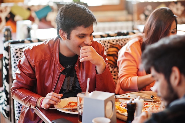 Gruppe asiatischer Freunde, die während einer Party in der Pizzeria Pizza essen Fröhliche indische Leute, die Spaß haben, zusammen italienisches Essen zu essen und auf der Couch zu sitzen