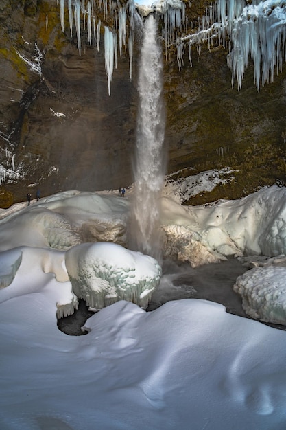 Gruppe Bergsteigertouristen hinter dem gefrorenen Kvernufoss-Wasserfall, mit Schnee und Stalagmiten w