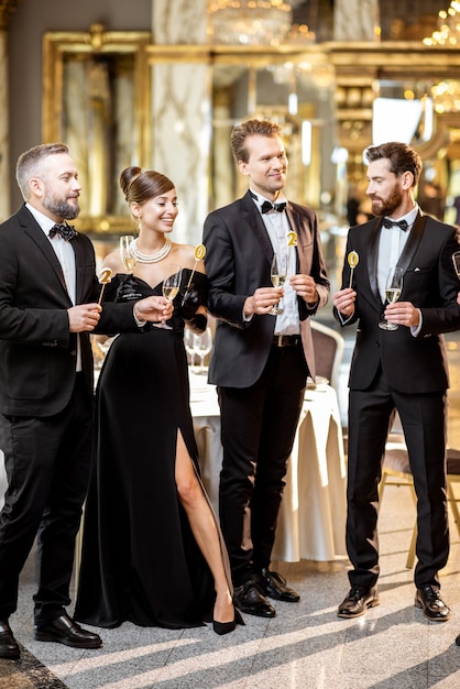 Gruppe eleganter Menschen, die im Retro-Stil gut gekleidet sind und Neujahr feiern und sich mit Weingläsern in der luxuriösen Restauranthalle amüsieren