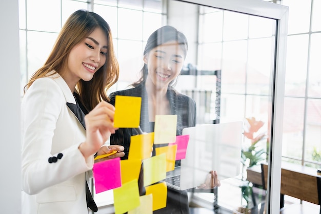 Gruppe erfolgreicher Teamwork asiatischer Geschäftsfrauen Brainstorming-Meeting mit bunten Haftnotizen an der Glaswand für neue Ideen mit agiler Methodik für Unternehmen in einem Tech-Startup-Büro