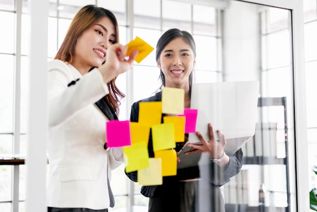 Gruppe erfolgreicher Teamwork asiatischer Geschäftsfrauen Brainstorming-Meeting mit bunten Haftnotizen an der Glaswand für neue Ideen mit agiler Methodik für Unternehmen in einem Tech-Startup-Büro