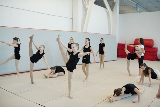 Gruppe flexibler Teenager-Mädchen, die beim Cheerleading-Training Split- oder Aufwärmübungen machen