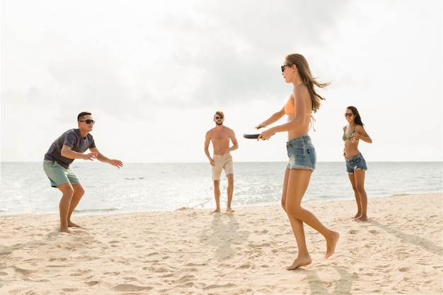 Gruppe Freunde, die am Strand an den Sommerferien spielen