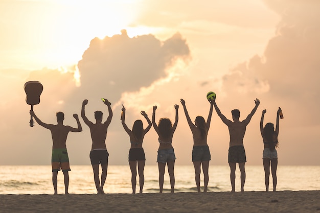 Gruppe Freunde, die Hände auf dem Strand bei Sonnenuntergang anheben