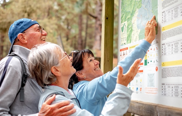 Gruppe fröhlicher älterer Freunde bei Bergausflügen, die auf der Karte in die richtige Richtung schauen und einen gesunden Lebensstil in der Natur genießen