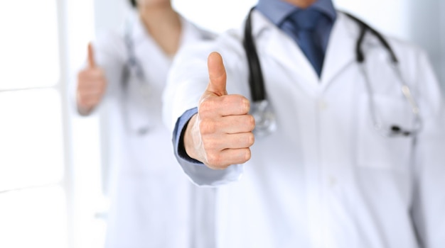 Gruppe fröhlicher Ärzte lächeln in die Kamera, Daumen hoch. Perfekter medizinischer Service in der Klinik. Glückliche Zukunft in der Medizin und im Gesundheitswesen.