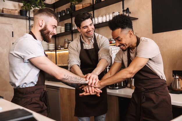 Gruppe fröhlicher Baristas, die Schürzen tragen, die an der Theke im Café drinnen arbeiten?