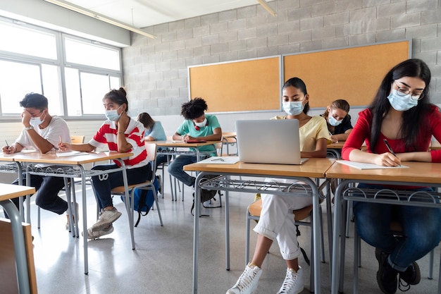 Gruppe gemischtrassiger jugendlicher Gymnasiasten, die Gesichtsmaske im Klassenzimmer tragen. Bildungskonzept.