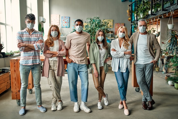 Gruppe gemischtrassiger Menschen, die während des Coronavirus in einem modernen Büro arbeiten. Junge Geschäftsleute und Senior-Chef arbeiten zusammen und tragen Gesichtsschutzmasken. Vorbeugende Maßnahmen während Covid-19