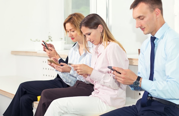 Gruppe Geschäftsleute untersuchen ihre Smartphones beim Sitzen im Büro.