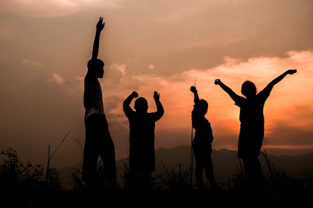 Gruppe glückliche kinder, die auf wiese bei sonnenuntergang, schattenbild spielen