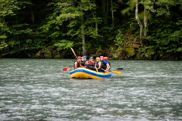 Gruppe glückliche leute mit dem führer whitewater, der auf fluss flößt und rudert.