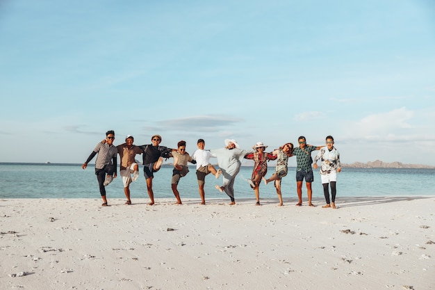 Gruppe glücklicher asiatischer Freunde, die Urlaub genießen, sich umarmen und am Strand tanzen?