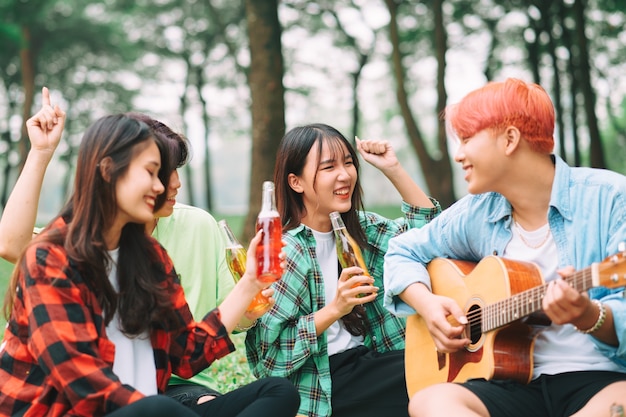 Gruppe glücklicher asiatischer junger Leute, die auf der Gitarre sitzen und im Park singen