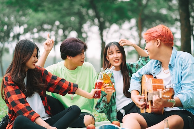 Gruppe glücklicher asiatischer junger Leute, die auf der Gitarre sitzen und im Park singen