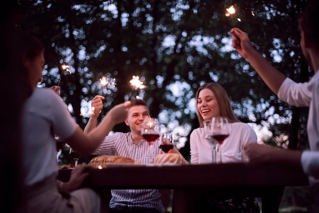 gruppe glücklicher freunde, die während der sommerferienferien in der nähe des flusses in der wunderschönen natur ein picknick-französisches abendessen im freien haben