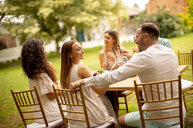 Gruppe glücklicher junger Leute, die frische Limonade trinken und Früchte im Garten essen