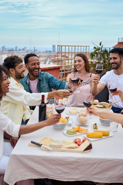 Gruppe glücklicher junger Leute, die Rotwein trinken und auf dem Dach feiern