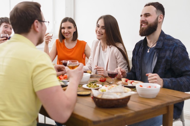 Gruppe glücklicher junger Leute lachen und plaudern am Esstisch, Party für Freunde drinnen im Café oder zu Hause. Freundschaft, Entspannung an Feiertagen und am Wochenende. Männer und Frauen sitzen am Tisch mit verschiedenen Gerichten.