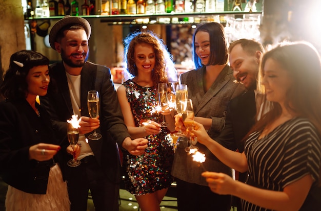 Gruppe glücklicher Menschen, die Wunderkerzen auf der Party halten. Junge Freunde, die mit Champagner anstoßen.